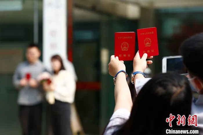 2021年5月20日，一对新人手持结婚证在北京海淀区民政局婚姻登记处外拍照留念。<a target='_blank' href='/'>中新社</a>记者 富田 摄 